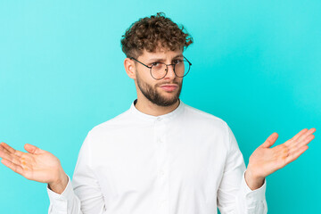 Wall Mural - Young handsome caucasian man isolated on blue background With glasses and having doubts