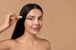 Beautiful woman applying serum onto her eyelashes on beige background, space for text. Cosmetic product