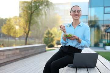 Poster - Smiling businesswoman with lunch box sitting near laptop outdoors. Space for text