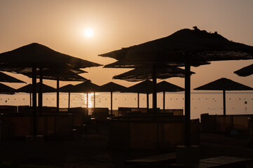 sunrise on the beach, umbrellas shadows and sun over the sea