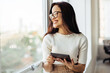 © (JLco) Julia Amaral - Business woman holding a tablet and standing next to a window