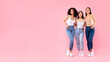 Portrait of three young diverse ladies friends embracing and posing over pink background, panorama with free space