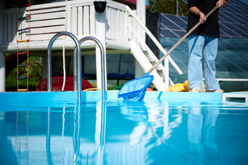 Wall Mural - Young woman cleans swimming pool. Personnel cleaning the pool from leaves in sunny summer day. Hotel staff worker cleaning the pool. Cleaning swimming pool service. Purification with a net. Close up