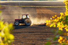 Tractor Plowing Field At Sunset Among Dust