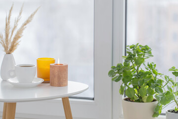 Poster - cup of coffee with burning candles  on white table by window on winter