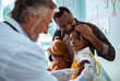 © Marko Geber - Young African American father embracing his daughter while she is getting a vaccine shot by the pediatrician at the hospital