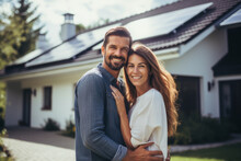 Happy couple standing in front of their house with solar panels installed on the roof. Alternative energy, saving resources and sustainable lifestyle concept.