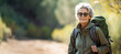 Senior female hiker wearing casual clothes taking a walk in autumn scenery. Adventurous elderly woman with a backpack. Hiking and trekking on a nature trail. Traveling by foot.