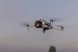 A small foldable drone in flight mode with the spot lights on.. A gray drone in flight in the air. Gray drone in flight in the air. quadrocopter with photo camera flying in the sky.