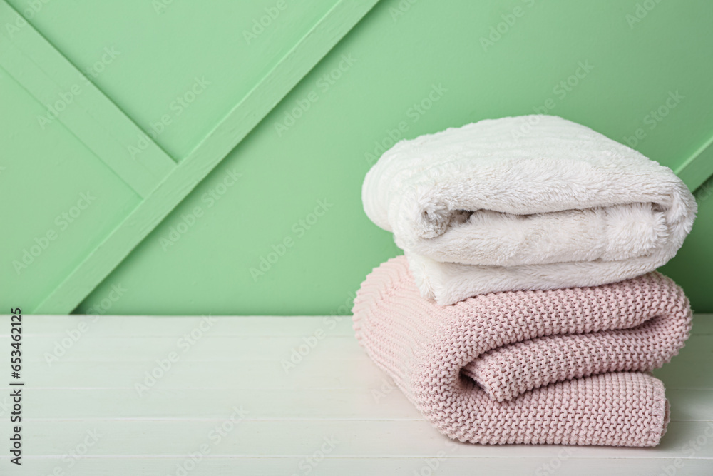 New soft folded blankets on light wooden table new green wall
