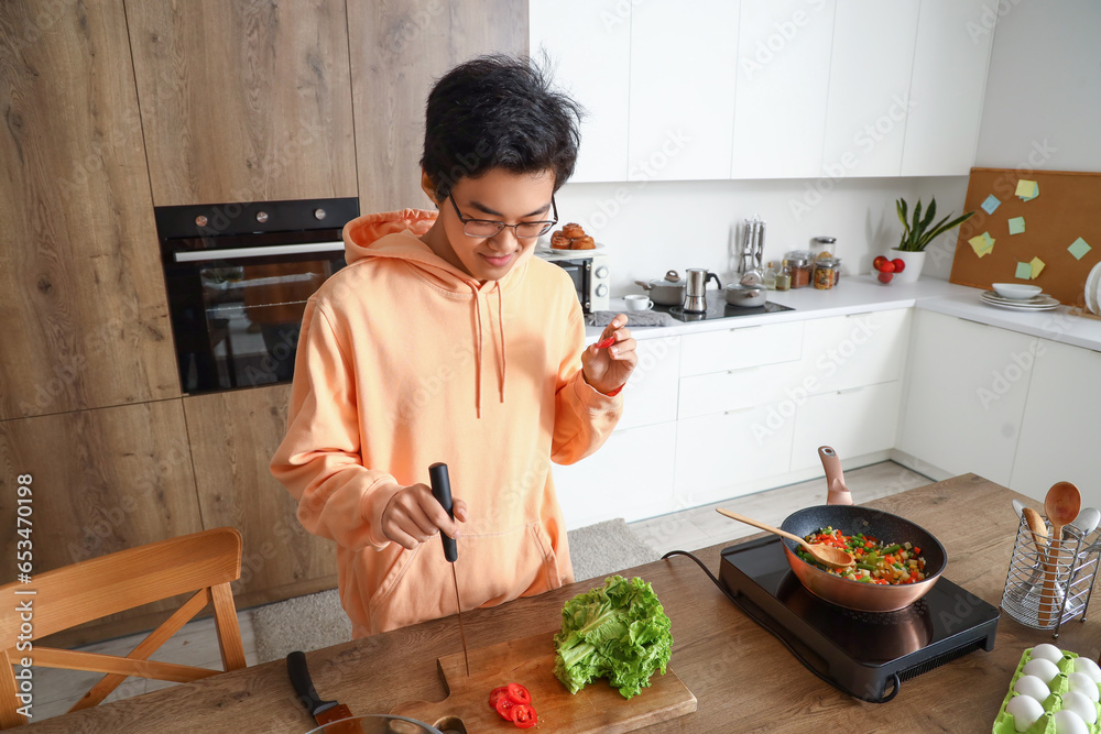 Young Asian man cutting tomatoes in kitchen