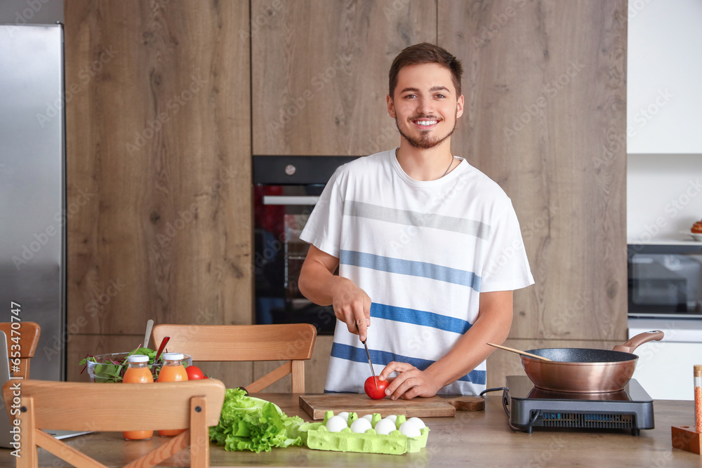 Young man cutting tomato in kitchen