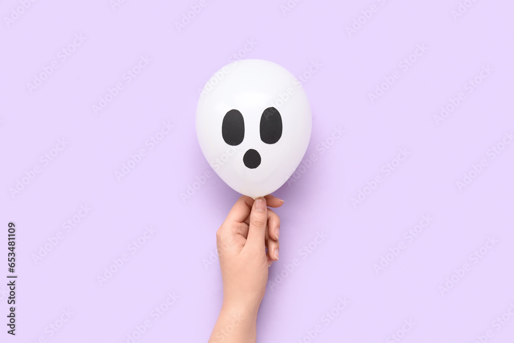 Female hand with funny Halloween white balloon on lilac background