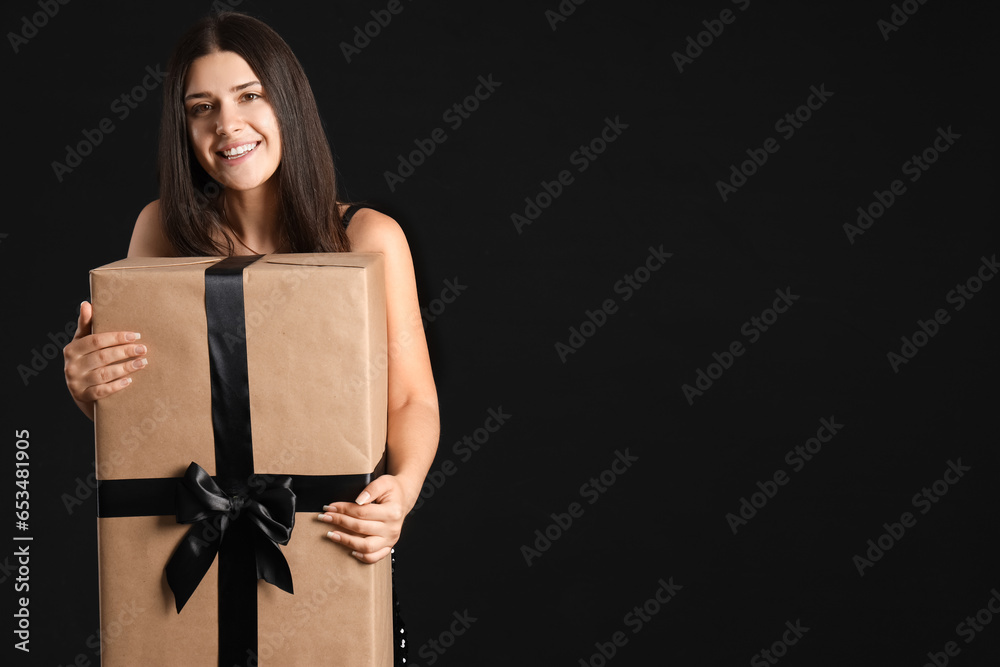 Young woman with gift box on dark background. Black Friday sale