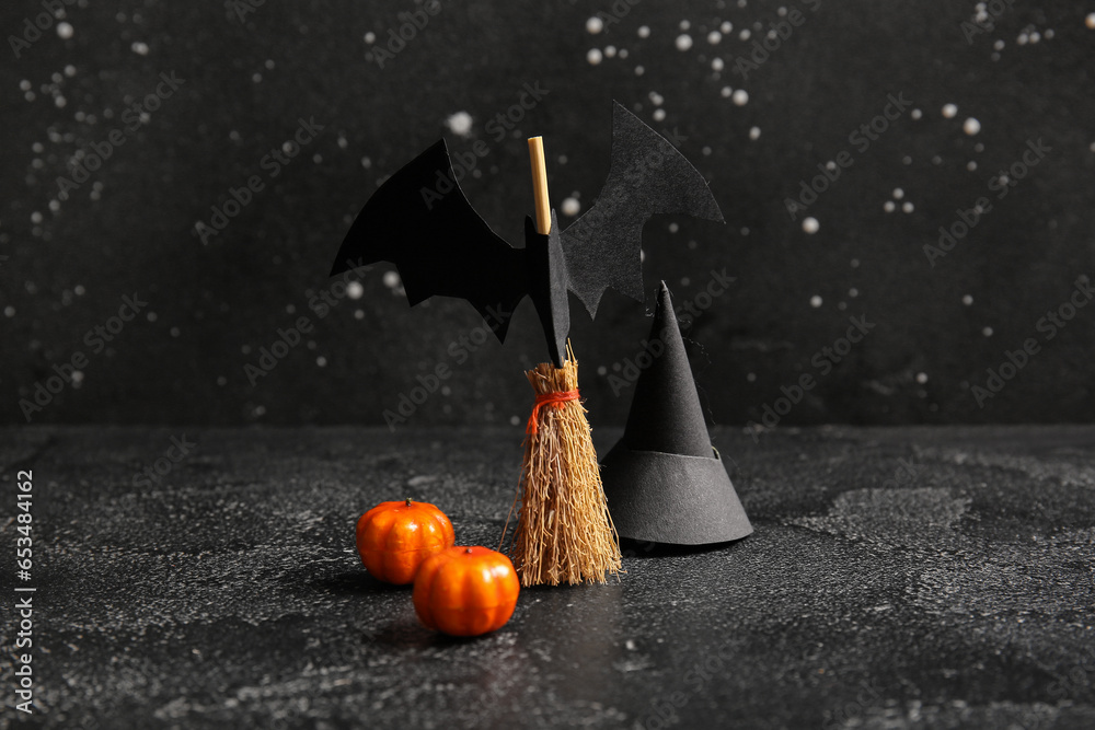 Halloween composition with broom, pumpkins, bat and witch hat on black grunge background