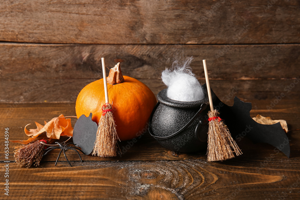 Halloween composition with brooms, pumpkins and cauldron on brown wooden background