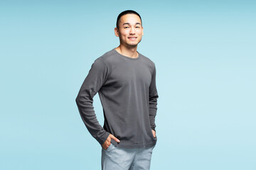 Positive asian man wearing long sleeve t shirt posing isolated on blue background, looking at camera