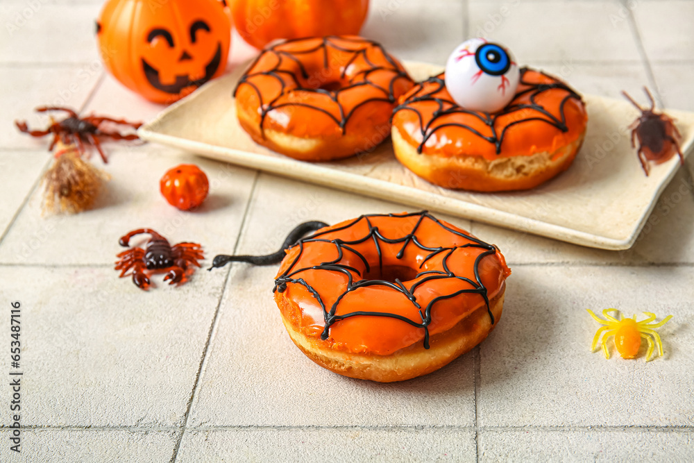 Tasty donuts with decorations for Halloween on white tile background
