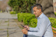 © jroballo - Young Latino man making a purchase with a credit card on his mobile phone sitting on a bench in a public park.