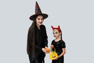 Canvas Print - Little girl with her mother dressed for Halloween and candies on light background