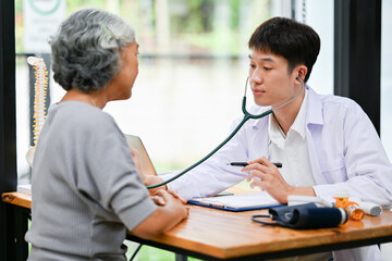 Wall Mural - A professional Asian male doctor is listening to a patient's heartbeat with a stethoscope.