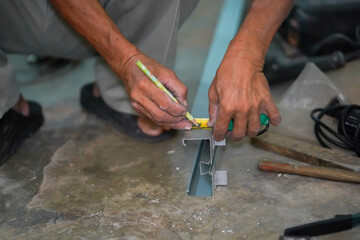 Closeup hands of builder using a pencil marks out the details before cutting aluminum lumber at construction site.