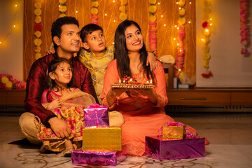 happy young indian family in traditional dress with lots of gifts around sitting on floor celebratin