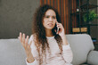 © ViDi Studio - Young sad upset woman wearing casual clothes sits on grey sofa couch talking speak on mobile cell phone stay at home hotel flat rest relax spend free spare time in living room indoor. Lounge concept.
