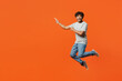 © ViDi Studio - Full body young fun smiling happy Indian man he wears t-shirt casual clothes jump high look camera point index finger aside isolated on orange red color background studio portrait. Lifestyle concept.