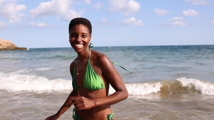 Wall Mural - Cheerful smiling black woman in bikini running out the sea water at the beach