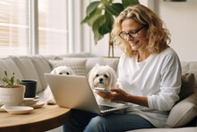 Happy middle-aged woman using laptop with her dog at cozy home.