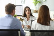 © H_Ko - Portrait of joyful businesswoman working at modern workplace with friendly clients. Woman listening attentively customer wishes. Biz negotiations concept