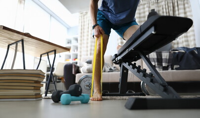 Low angle of person training with yellow fitness rubber band. Indoors gym with necessary equipment for sport workout. Colourful dumbbells. Health and active lifestyle concept