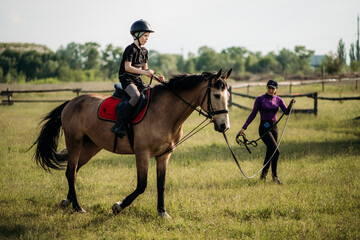 a teenage boy in a helmet learns horse riding in the summer, the instructor teaches the child equest