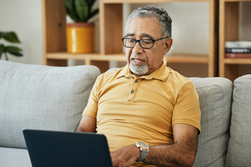 Canvas Print - Senior man, typing and laptop on sofa in home with online research in living room or streaming video, movies or tv show. Elderly, person or writing on computer in retirement for blog or communication