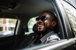 A smiling African-American businessman is riding in the back seat of a car. 