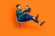 Leinwandbild Motiv Full body cadre of young man sitting chair steering wheel driver excited drunk alcoholic accident crash isolated on orange color background