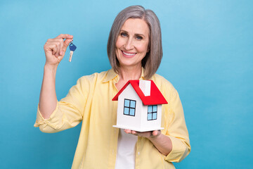 Sticker - Photo of positive aged lady toothy smile arm hold showing little house key isolated on blue color background