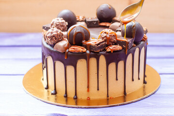 Close up of woman's hand pouring salted caramel sauce on the chocolate cake, decorated with sweets, truffles, cookies and nuts