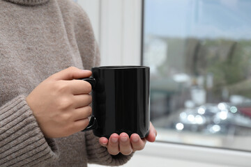 Canvas Print - Woman holding black mug indoors, closeup. Mockup for design