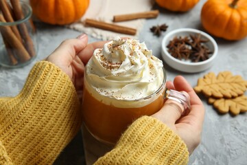 Wall Mural - Woman holding cup of pumpkin spice latte with whipped cream at light grey table, closeup