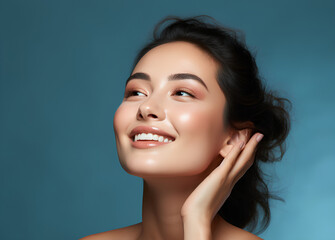 Skin care. Woman with beauty face touching healthy facial skin portrait. Beautiful smiling asian girl model with natural makeup touching glowing hydrated skin on blue background closeup 