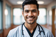 portrait shot of young age indigenous male doctor in doctors outfit looking at camera while standing in the hospital, sly smile, blurred background