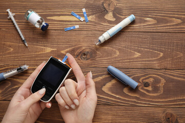 Wall Mural - Diabetic woman using glucometer on wooden background