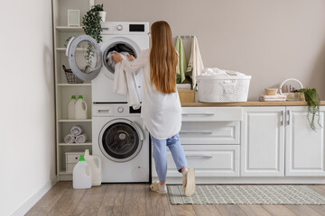 Wall Mural - Woman putting dirty clothes into washing machine in laundry room