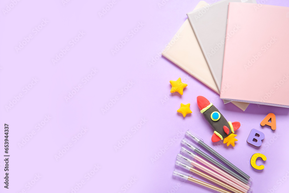 Rocket made of plasticine with different stationery on lilac background