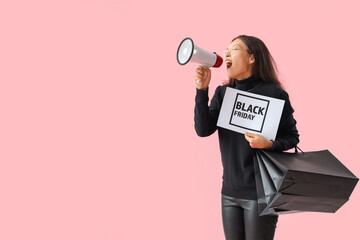 Wall Mural - Young Asian woman with shopping bags shouting into megaphone on pink background. Black Friday sale