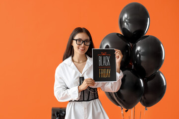 Canvas Print - Young Asian woman with card and balloons on orange background. Black Friday sale