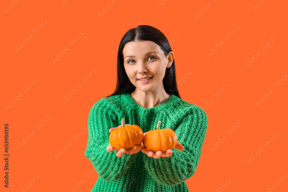 Beautiful woman with pumpkins on orange background