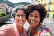 © Bougie Banana - Interracial middle age couple of friends or lesbian travelers in city, summer vacation